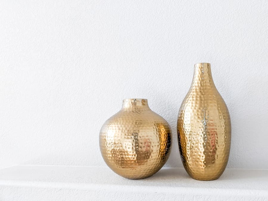 Two textured golden decorative vases against a soft white wall